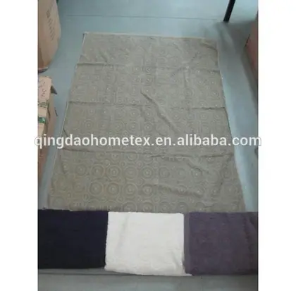 Patterned floor mat laid flat on warehouse floor beside cardboard boxes, with folded fabric swatches at the bottom edge
