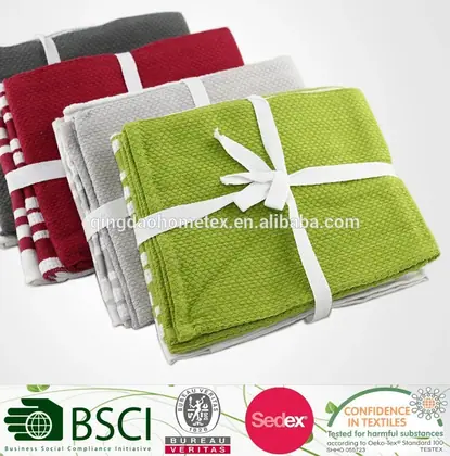 Folded cotton kitchen towels in grey, red, striped and green tied with white ribbons, certification logos banner below