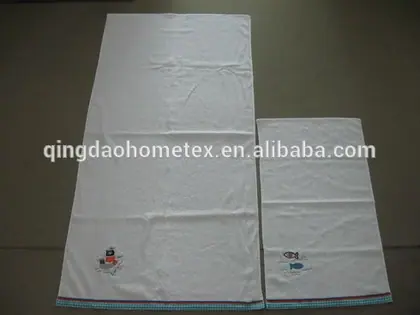 Two white towels with small embroidered motifs and checkered border trim laid flat on a gray surface