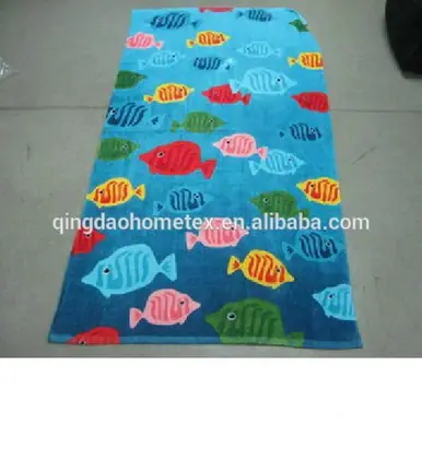 Blue beach towel printed with colorful tropical fish pattern laid flat on a gray concrete floor