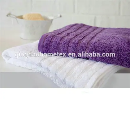 Folded purple towel stacked on a white towel beside a white tub with a sponge against a white brick wall