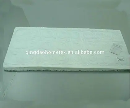 White bath mat with embossed circular pattern photographed at an angle on a plain grey surface