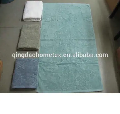 Large mint-green towel laid flat next to three folded towels in white, sage green, and blue on a tiled floor