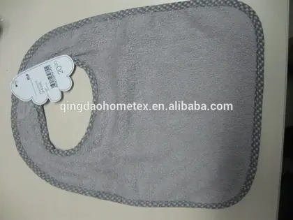 Gray terry cloth baby bib with checkered trim and paper hang tag lying on a plain light surface