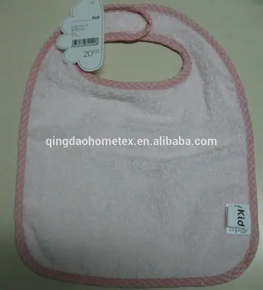 Pink terry baby bib with gingham trim and hanging loop, price tag attached, lying on a beige surface
