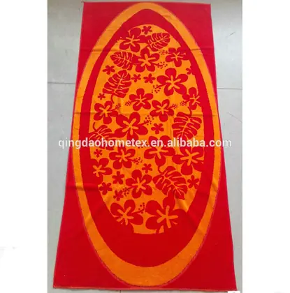 Red beach towel with orange oval panel printed with red hibiscus flowers and leaves, lying on a beige tiled floor