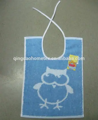 Blue terry baby bib with white owl print and tie strings lying on a gray floor