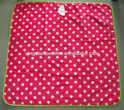 Pink fleece blanket with white star print and green binding laid flat on floor