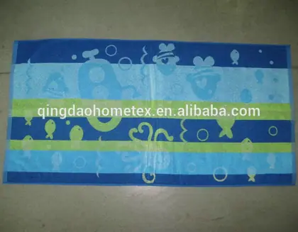 Blue and green striped beach towel printed with fish and sea creatures, laid flat on a concrete floor
