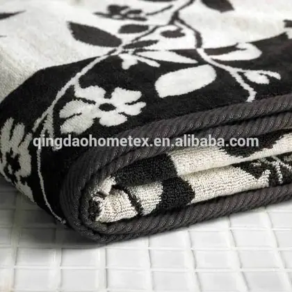 Folded black and white floral jacquard towel with dark trim lying on white tiled surface