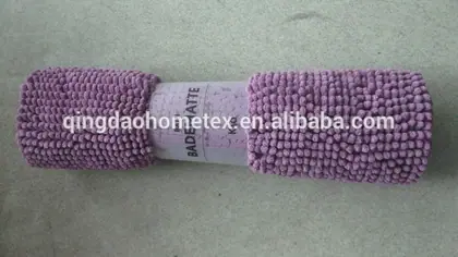 Rolled lilac chenille bath mat with paper band labeled BADEMATTE on plain beige surface