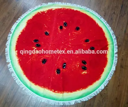 Round watermelon-printed beach towel with fringe tassels laid flat on a wooden floor