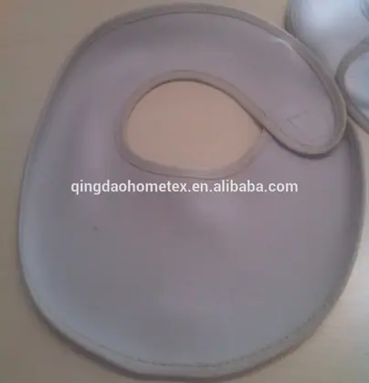 Light beige fabric baby bib with neck opening and fastening tab, partly folded, photographed on a table