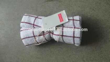 Rolled white kitchen towel with red grid pattern and hang tag on concrete floor