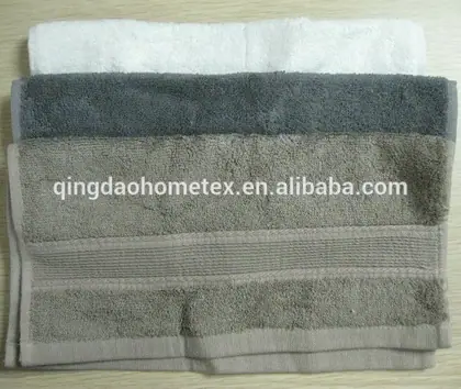 Stack of three folded towels in white, gray, and beige on a wooden surface