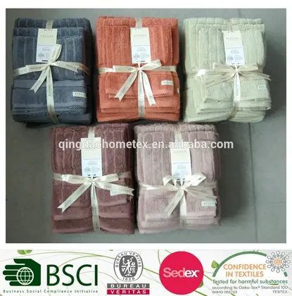 Five towel sets in grey, coral, cream, dusty rose and pink, tied with ribbons and tags, plus certification logos below