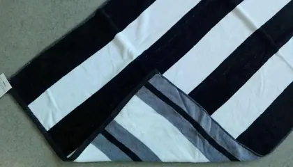Folded black and white striped beach towel with gray stripe border lying on a plain gray surface