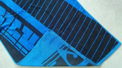 Blue and black striped beach towel with printed graphic design, laid on a gray surface
