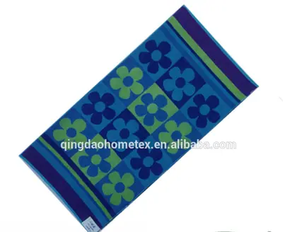 Printed beach towel with blue and green flower pattern, shown diagonally, with BSCI and OEKO-TEX certification logos below