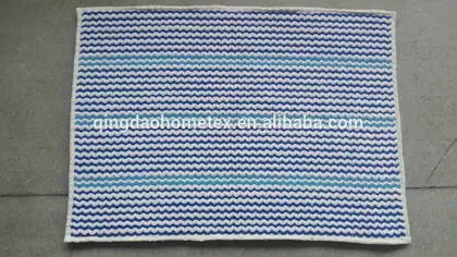 Rectangular woven mat with blue and white zigzag stripes and light blue accent stripes, laid on a gray concrete floor