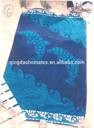 Blue beach towel with mosaic-style dolphin and wave pattern laid on sand with seashells