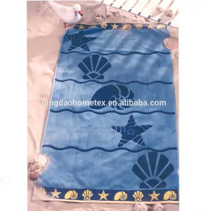 Blue beach towel with navy seashell and starfish patterns and a yellow shell border, laid on sand with seashells and a toy seagull