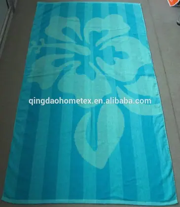 Teal beach towel with darker blue stripes and a large hibiscus flower print, laid flat on a floor