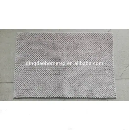 Light gray chenille bath mat with pebbled texture lying on a concrete floor