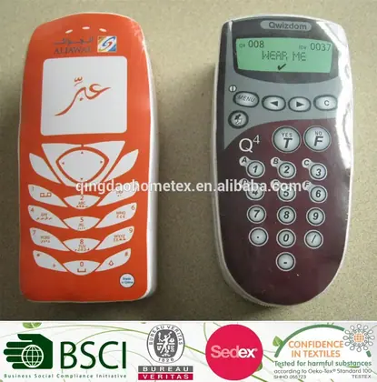 Two phone-shaped fabric items, one orange with Arabic text and one dark red remote-style, on a beige surface with certification logos below