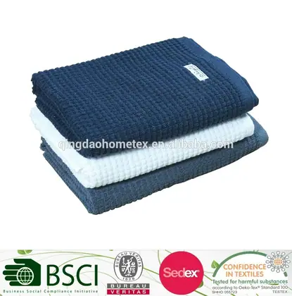 Stack of three waffle-weave towels in navy blue, white, and blue with a small label, on a white background