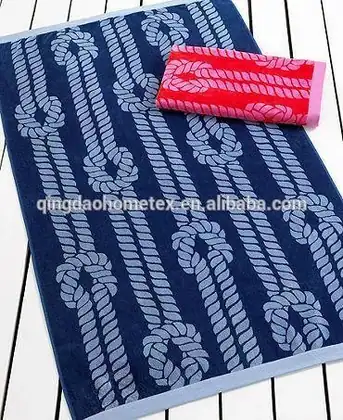 Navy blue beach towel with rope-knot print and a folded red towel on a white slatted surface