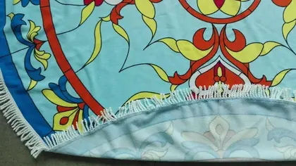 Close-up of a round fringed beach towel with a colorful floral mandala print in blue, red, and yellow
