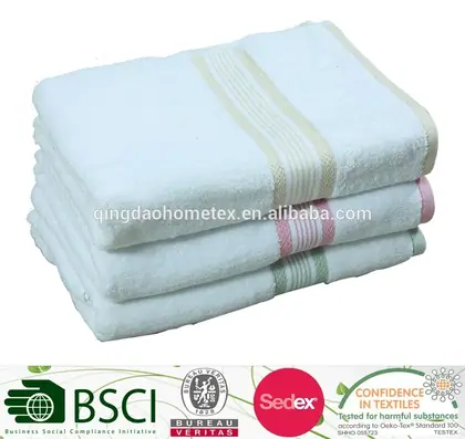 Stack of folded white terry towels with striped borders, with certification logos along the bottom edge