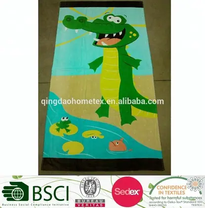 Printed beach towel featuring a cartoon green crocodile on a beach with fish and lily pads, shown flat on a surface
