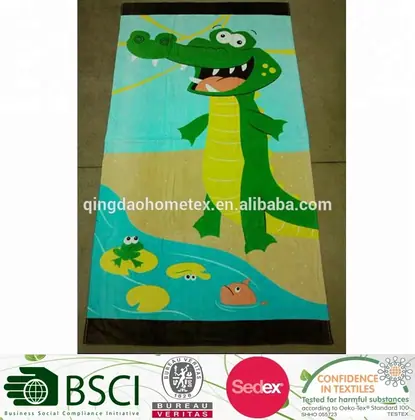 Printed beach towel with a cartoon green crocodile design lying on a tiled floor