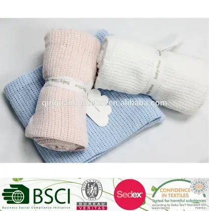 Rolled knitted baby blankets in pink, white, and blue with brand labels, certification logos below
