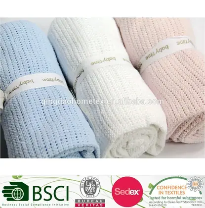 Three rolled knitted baby blankets in blue, white, and pink with paper bands, plus certification logos below