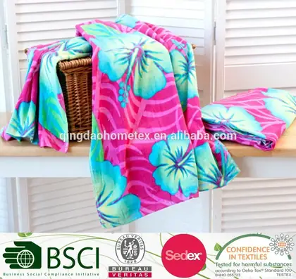 Pink and teal floral-printed beach towels draped over a wicker basket, with a certification banner strip at the bottom.