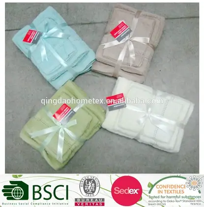 Four sets of folded embroidered towels in pastel colors, each tied with ribbon and tags, on a concrete floor