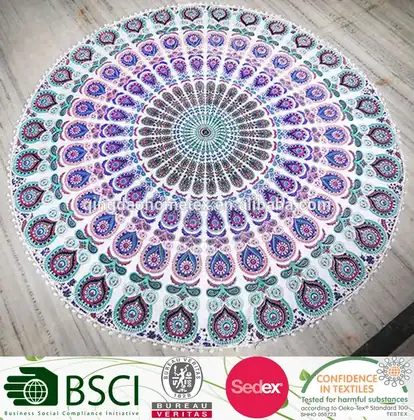 Round mandala tapestry in purple, teal, and pink with pom-pom trim, laid flat on a wooden floor