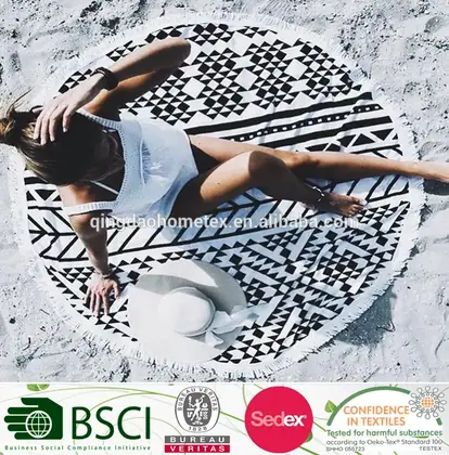 Woman lying on a round black-and-white geometric patterned beach towel on sand, with white hat; certification logos below