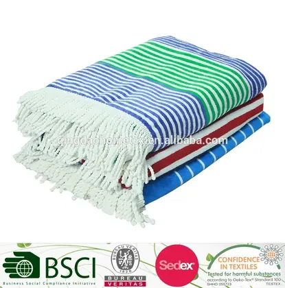 Stack of folded striped woven towels with white fringe in blue, green, and red, on white background with certification logos below