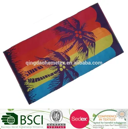 Colorful beach towel with purple palm tree print on rainbow stripes, tilted on white background
