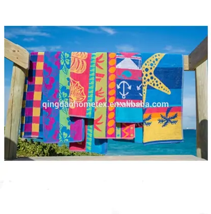 Colorful patterned beach towels with starfish and anchor designs hanging on a wooden rail by the sea