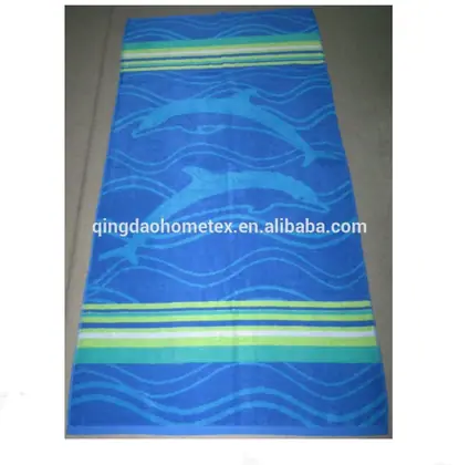 Blue beach towel with dolphin print and green striped borders, laid flat on a gray floor