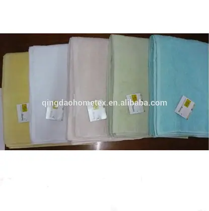 Five folded towels in yellow, white, pink, green, and teal with attached tags on a dark surface