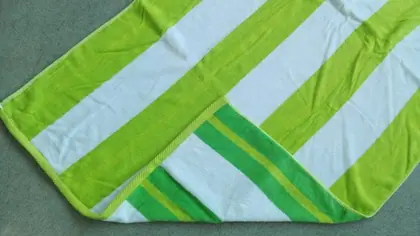 Folded green and white striped beach towel lying on a plain surface