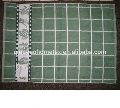 Green checkered kitchen towel with white grid pattern and decorative vegetable-print border on dark carpet background