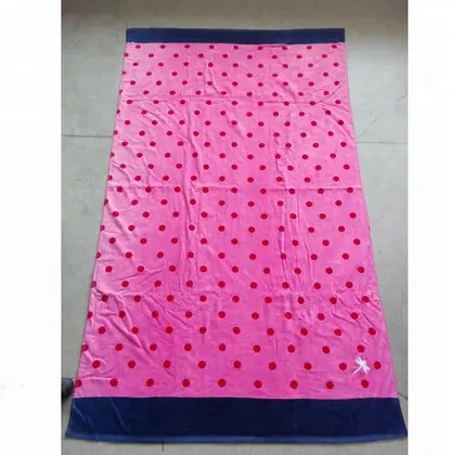 Pink beach towel with red polka dots and navy blue borders laid flat on a tiled floor