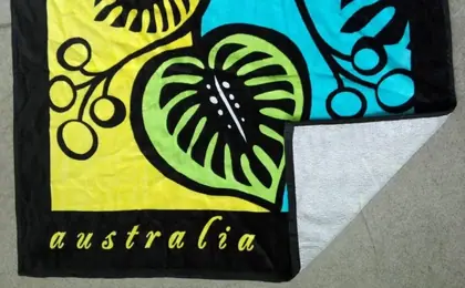 Folded beach towel with black border, colorful leaf print in yellow, blue and green, and the word 'australia' printed on the border